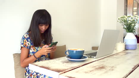 Attraktives-Brünettes-Asiatisches-Mädchen,-Das-Mit-Ernstem-Gesicht-Am-Tisch-Im-Café-Sitzt-Und-SMS-Auf-Dem-Smartphone-Schreibt