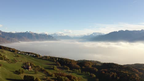 Flying-high-over-farm-fields-revealing-Vevey,-Montreux-and-Lake-Léman-below-the-mist,-sunset-light