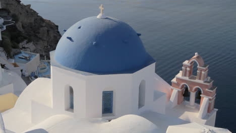 Die-Berühmte-Blaue-Kirchenkuppel-Mit-Der-Rosafarbenen-Kirchenglocke-In-Oia,-Santorini