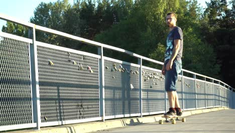 Young-man-skating-on-the-longboard-over-the-bridge-with-locks-having-fun
