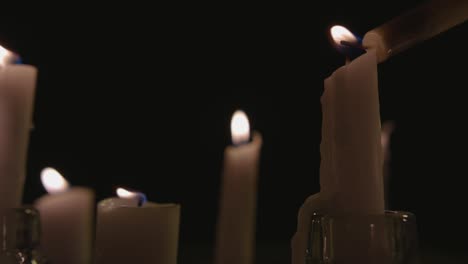 Eine-Extreme-Nahaufnahme-Und-Ein-Schwenk-über-Weiße-Kerzen,-Die-Vor-Schwarzem-Hintergrund-Beleuchtet-Sind