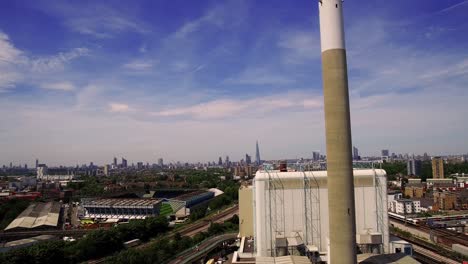 Aerial-view-of-Lewisham-recycling-centre-and-Millwall-FC,-descending-shot-with-Londons-skyline-in-the-background