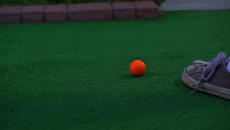 An-orange-ball-getting-hit-by-a-putter-at-a-miniature-golf-course