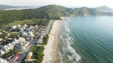 Filmische-Luftaufnahme-Mit-Einer-Drohne-Eines-Strandes-Mit-Dschungelbergen-Am-Horizont-Einer-Brasilianischen-Küste,-Mariscal,-Santa-Catarina,-Brasilien