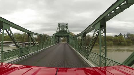 Red-vehicle-traveling-over-big-steel-bridge
