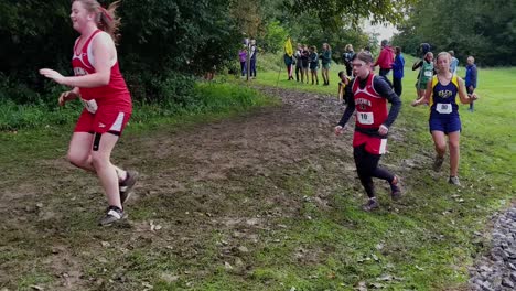 Several-female-cross-country-runners-slip-and-fall-on-bend,-junior-high-running-competition,-wet-and-slippery-xcountry-trail-in-forest