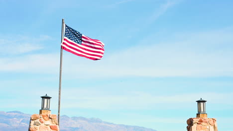 Bandera-Americana-Que-Sopla-Por-El-Viento-Con-Dos-Polos-Al-Lado-Y-Fondo-De-Cielo-Azul