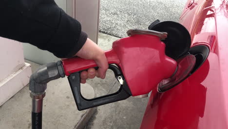 Hält-Eine-Rote-Zapfsäule-In-Der-Hand,-Während-Sie-Benzin-Aus-Fossilen-Brennstoffen-In-Ein-Auto-Pumpt