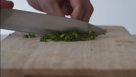 Hands-cutting-parsley-with-a-knife-over-a-chopping-board-in-4k