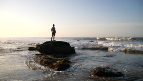 Ein-Mann-Steht-In-Einer-Epischen-Pose-Und-Beobachtet-Den-Sonnenaufgang-In-Friedlicher-Meditation,-Während-Die-Meereswellen-Am-Strand-In-Santa-Barbara,-Kalifornien,-In-Zeitlupe-Krachen