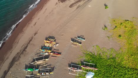 drone-aerial-of-fishing-pump-boats-on-a-sandy-beach-as-waves-come-ashore-on-a-sunny-day