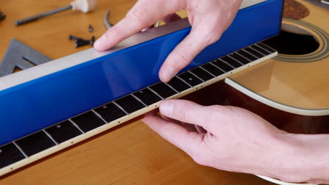 Close-up-hands-of-a-luthier-sanding-and-leveling-the-frets-on-an-acoustic-guitar-neck-fretboard-on-a-wood-workshop-bench-with-lutherie-tools