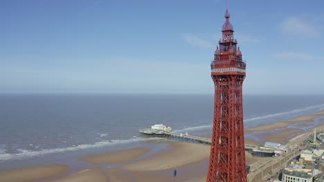 Aerial-footage,-drone-view-,-of-the-famous-Blackpool-Tower-and-beach-from-the-sky-on-a-beautiful-Summers-day-on-one-of-Great-Britains-most-popular-holiday-destinations,-tourist-attractions-by-the-sea