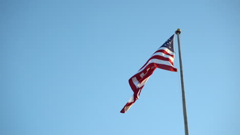Bandera-Estadounidense-En-Un-Asta-De-Bandera-Contra-El-Cielo-Azul,-Moviéndose-Lentamente-En-El-Viento