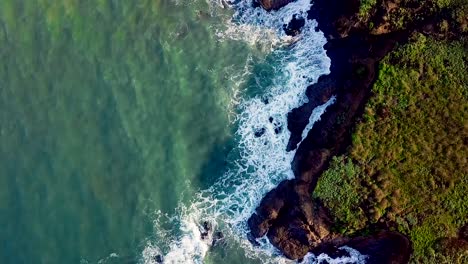 Aerial-shot-turning-above-sunlit-waves-crashing-into-rocky-California-cliffs