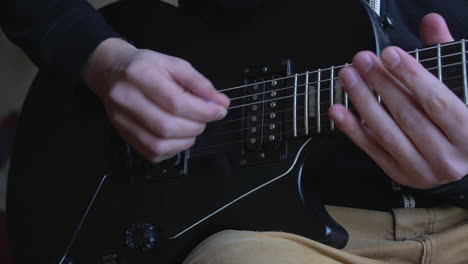 Mann,-Der-Eine-Schwarze-Vintage-E-Gitarre-übt-Und-Akkorde,-Soli-Und-Oktaven-In-Einer-Umgebung-Mit-Natürlichem-Licht-Einstudiert.