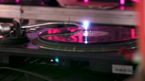 Close-shot-of-a-the-turntable-of-a-dj-moving-in-slow-motion-in-a-party-with-pink-lights