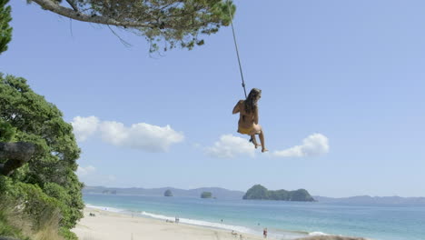 Girl-on-rope-swing-on-hahei-Beach,-New-Zealand