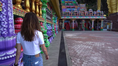 Women-walking-towards-the-Batu-caves-with-camera-tilting-up-to-reveal-the-giant-colorful-staircase-in-Selangor,-Malaysia