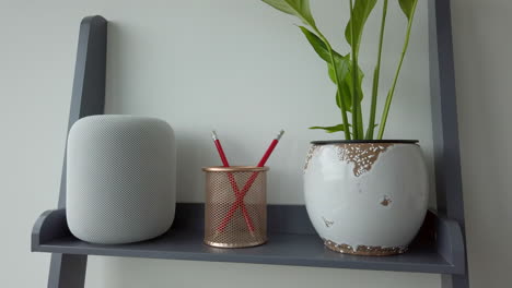 Slow-Motion-Static-Shot-of-Man-Single-Tapping-an-Apple-HomePod-on-top-of-Modern-Looking-Bookshelf-adjacent-to-a-Pencil-Holder---Plant
