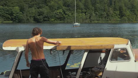 Youth-topless-wipes-down-sanded-roof-of-wooden-boat-before-varnishing