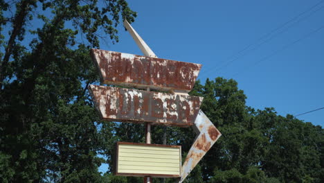 Gimbal-approach-shot-of-a-rusty-retro-lumber-store-sign-on-a-deserted-dirt-road-on-a-bright-sunny-day
