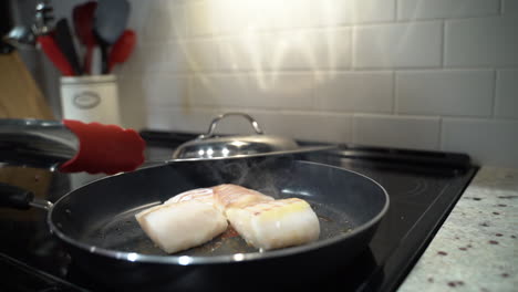 Fish-frying-in-a-pan-when-a-woman-reaches-in-to-flip-with-a-metal-tongs