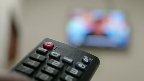 Hand-closeup-of-the-man-with-the-remote-control-and-watching-the-television-with-presses-to-change-the-channel-on-the-button