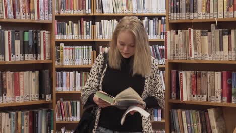 Smiling-girl-is-walking-towards-camera-in-library-between-bookshelves