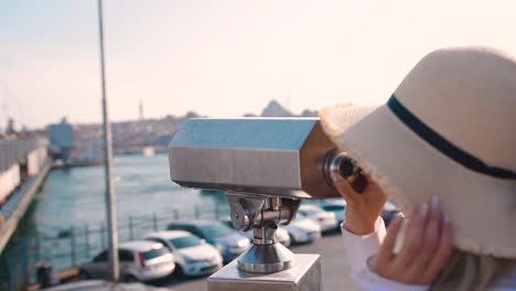 Slow-Motion:Beautiful-young-girl-looks-through-sightseeing-binoculars-with-view-of-Galata-Tower-and-Eminonu-district-in-Istanbul,Turkey