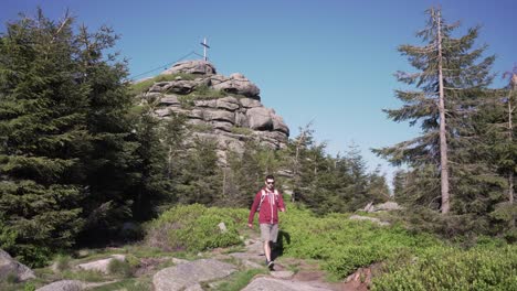 Adult-man-is-hiking,-wooden-cross-at-the-top-of-a-rock-in-a-background,-cinematic-shot