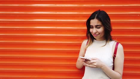 Zeitlupe:-Schönes-Junges-Mädchen-Verwendet-Smartphone-Und-Text-Mit-Orangefarbenem,-Rotem-Hintergrund