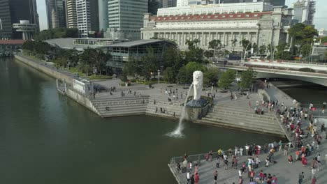Flying-around-the-famous-merlion-statue,-symbol-of-singapore,-surrounded-by-crowd-of-traveling-tourists-in-the-metropolis-city-center