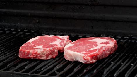 A-raw-rib-eye-steak-is-placed-on-a-grill-next-to-another-one