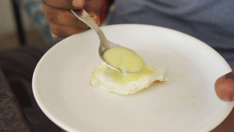 Dark-skinned-hungry-Asian-man-eating-poached-egg-with-spoon,-slow-motion