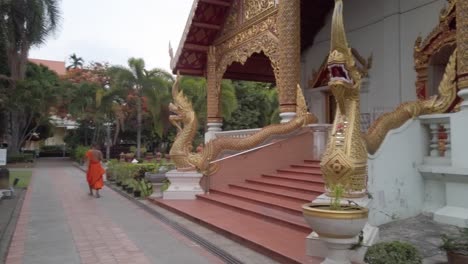 Slow-pan-shot-to-reveal-the-impressive-golden-framed-entrance-of-the-Wat-Phra-Singh-Temple-including-two-incredibly-detailed-mythical-dragon-statues-and-a-young-monk-going-downstairs