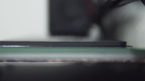 Super-close-up-with-a-shallow-depth-of-field-to-a-3D-printer-extruder-while-working,-with-black-PLA-filament-and-glass-heated-bed