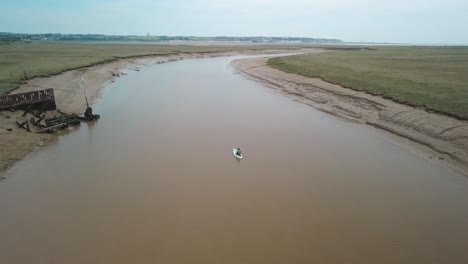Man-kayaking-on-meandering-river,-drone-follows-and-pans-up-to-reveal-beautiful-landscape-in-the-background