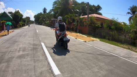 A-following-shot-of-a-man-riding-a-motorcycle-in-the-rural-streets-of-the-island-of-Bohol,-Philippines