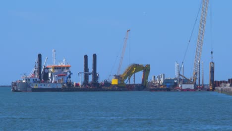 Hopper-dredger-ship-working-at-Port-of-Liepaja,-crane-with-bucket-lifts-up-soil-from-the-bay,-medium-shot-from-a-distance