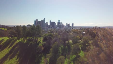 Fly-over-grassy-hill-to-reveal-urban-park-and-downtown-Los-Angeles-skyline