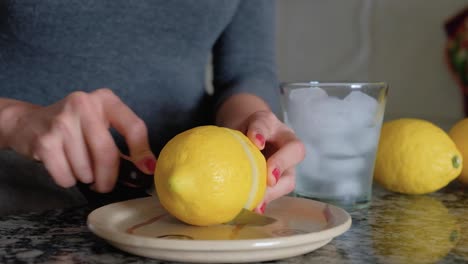 Frau-Schneidet-Eine-Zitrone-Mit-Einem-Messer-Und-Einem-Glas-Limonade-Daneben-In-Zwei-Hälften