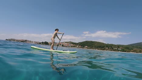 Bikini-woman-stand-up-surfboard-rowing-in-Sithonia,-Greece,-tracking