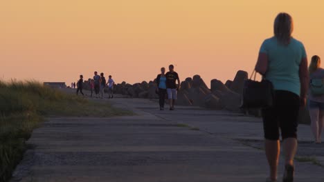 Gente-Caminando-En-El-Muelle-Norte-De-Karosta-En-La-Romántica-Puesta-De-Sol-Roja-Brillante,-Plano-Medio-Desde-La-Distancia
