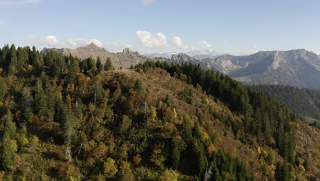 Sobrevolando-Una-Colina-Alta-Con-Excursionistas-En-La-Parte-Superior,-Revelando-Un-Paisaje-Alpino-En-El-Fondo