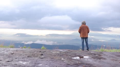 Young-man-standing-on-top-of-cliff-enjoying-view-of-nature
