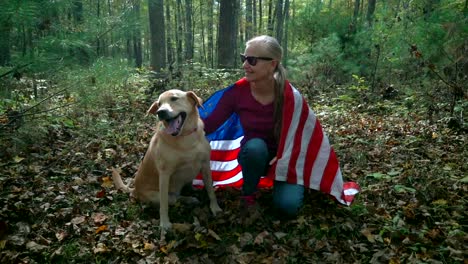 With-a-flag-draped-around-them-a-blonde-woman-pets-her-dog-and-the-dog-looks-up