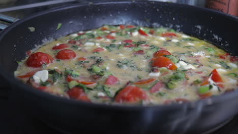 Slow-pan-sliding-shot-right-to-left-of-tomato,-red-pepper,-kale,-zucchini--courgette,-bacon-and-onion-omelette-frittata-cooking-in-frying-pan