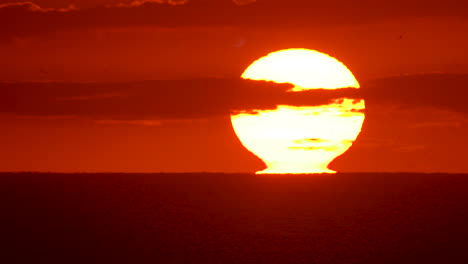 Closeup-of-a-sunrise-as-the-sun-rips-away-from-the-ocean-horizon,-glowing-the-sky-orange-and-pink