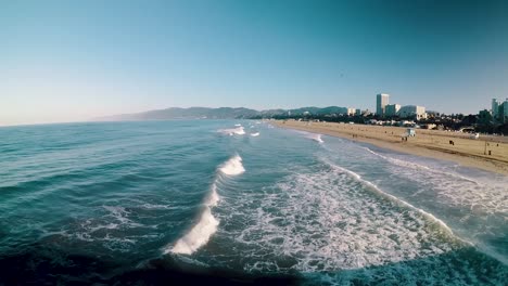 Point-of-View-from-pier-of-blue-waves-lapping-onto-California-beach-on-sunny-day